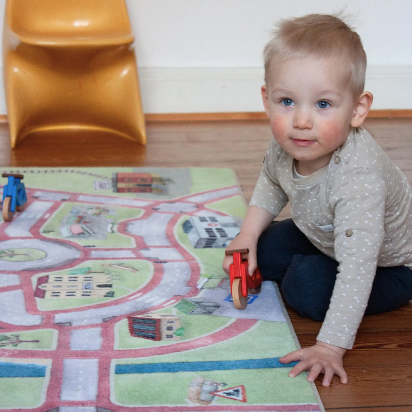 Kind mit rotem Holzfahrrad auf Spielteppich