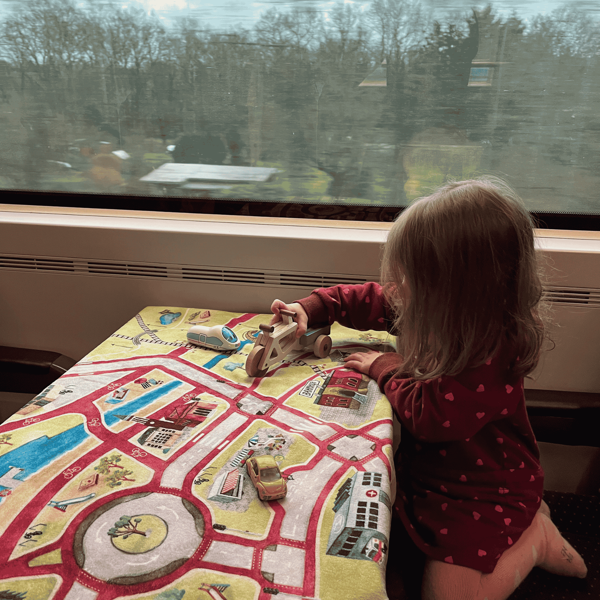 Child playing with toy cars on a colorful play mat while traveling by train.