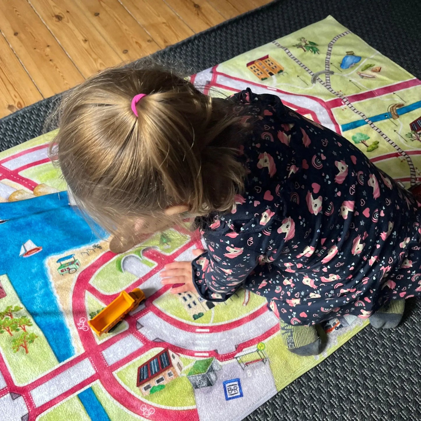 Child playing on colorful play mat, engaging with toy vehicle and road designs.