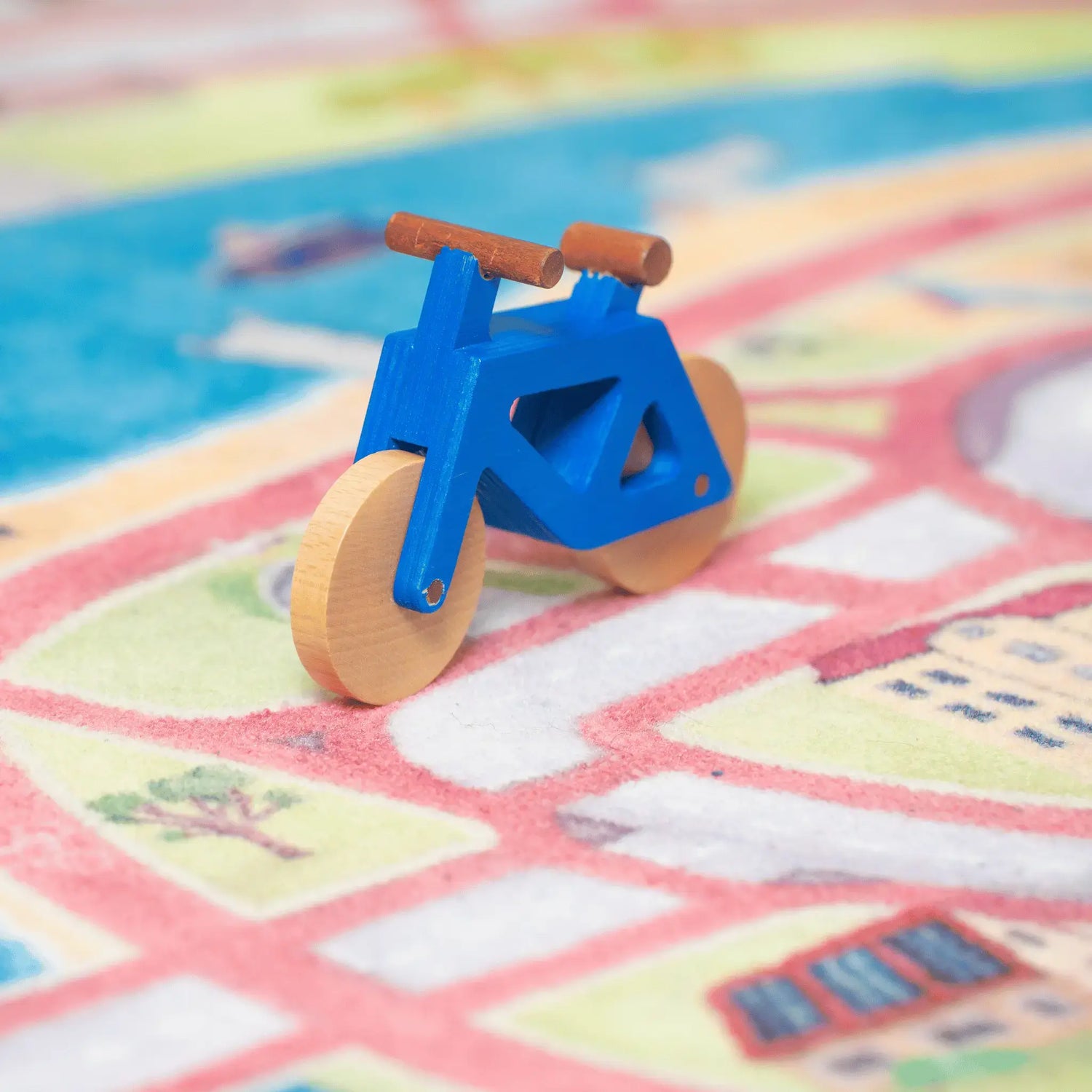 Das Spielwende Spielzeugfahrrad aus Holz in blau steht auf dem Spielteppich auf einem Radweg.