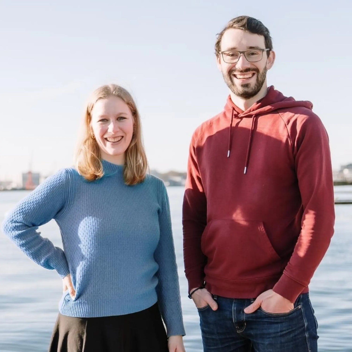 Lena Stöcker und Philipp Walter, die Gründer:innen von Spielwende, stehen nebeneinander an der Förde in Kiel